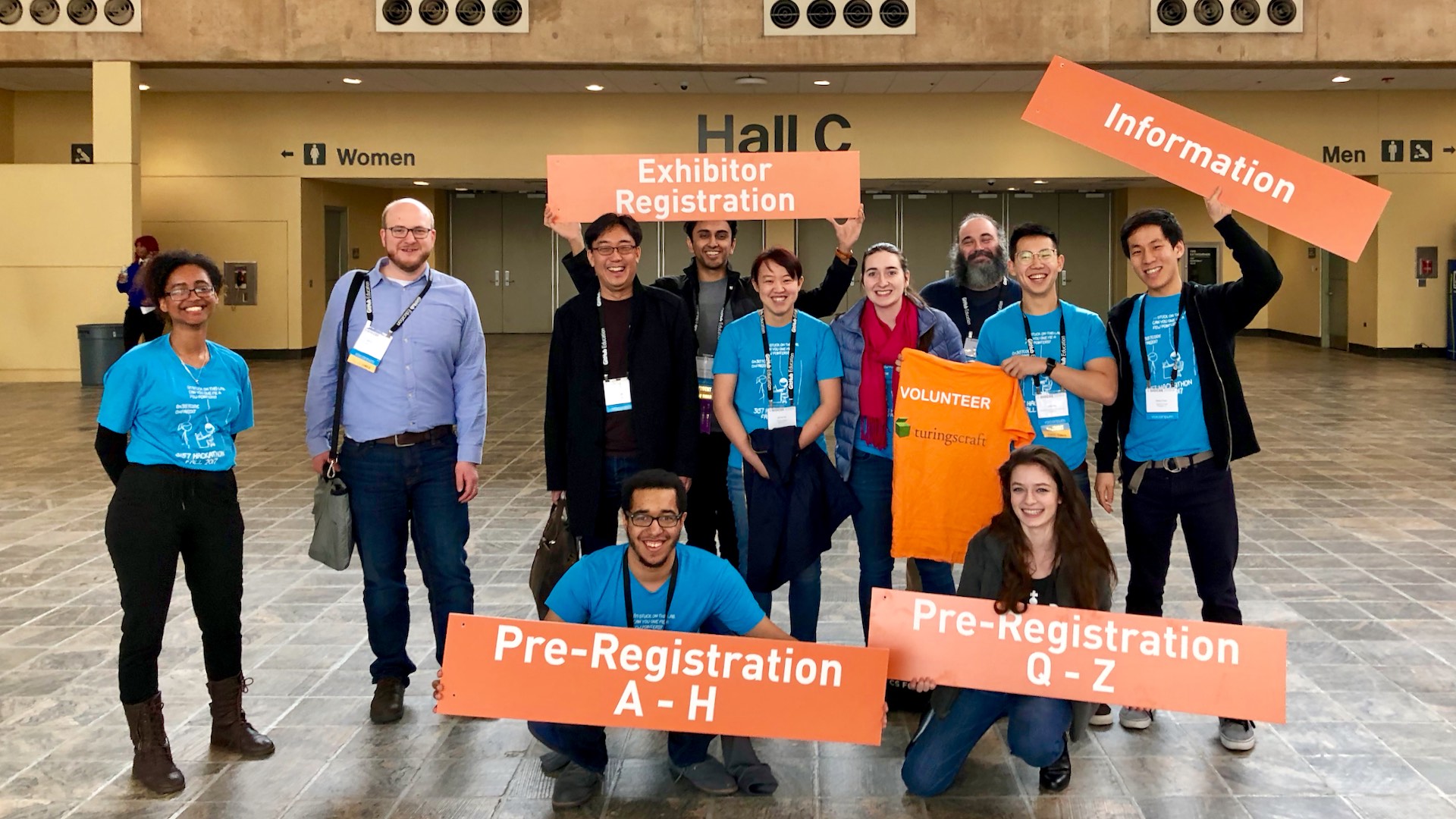 Twelve people smiling and holding various signs taken from the registration desk